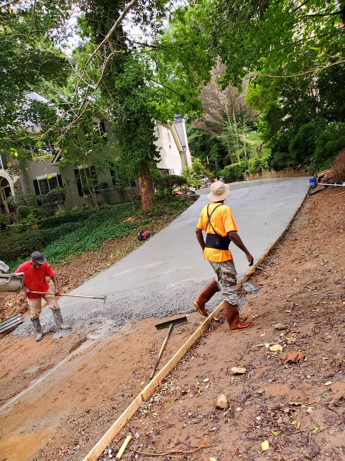 Two workers spreading and walking a fresh concrete driveway still in the wooden forms