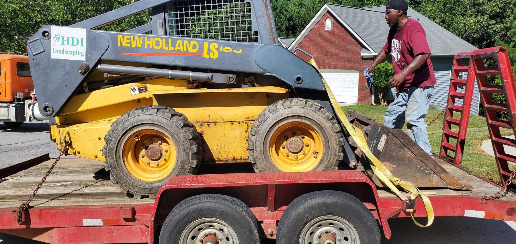 Skid steer strapped on a red flatbed trailer in front of a brick house